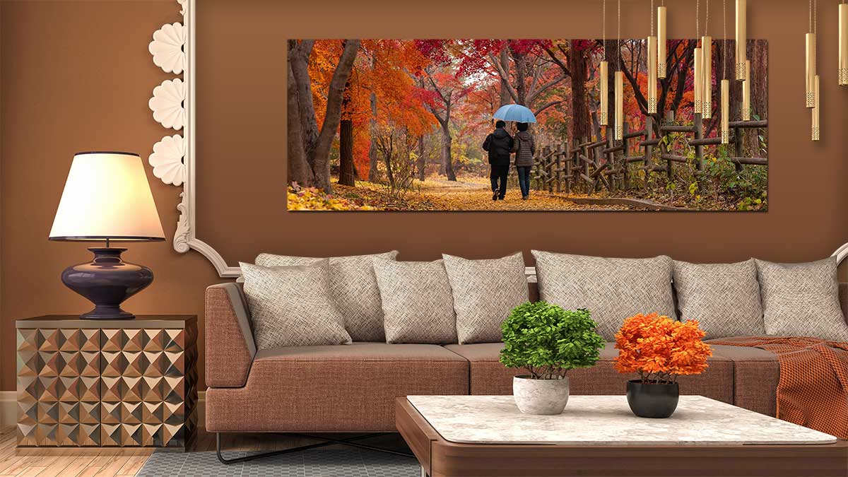 Picture of a couple walking amongst autumnal trees printed on a panoramic poster hung on a wall