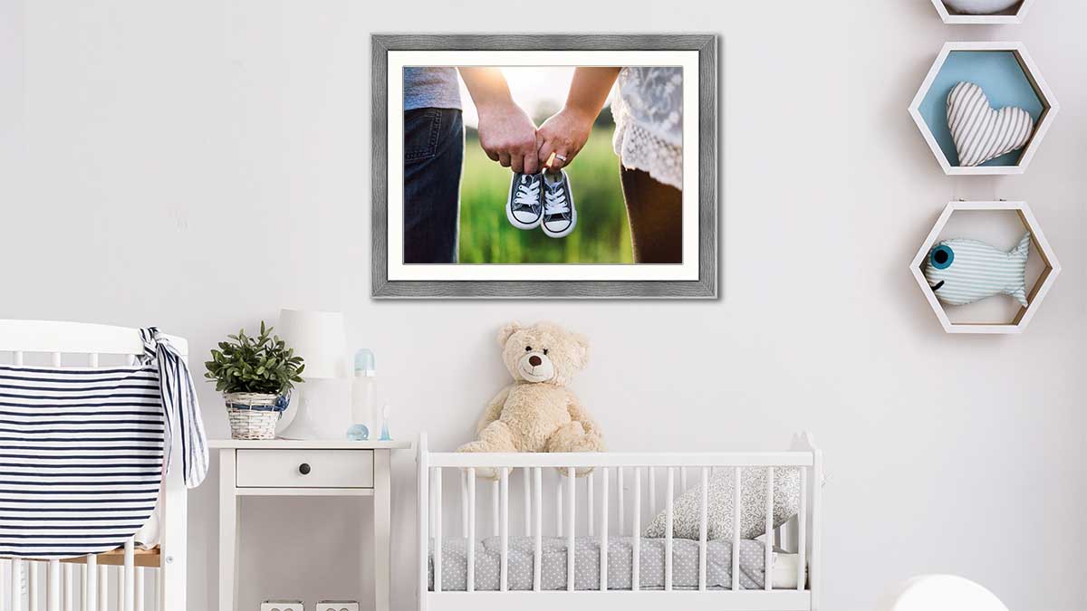 Photo of baby shoes in an A3 grey frame, hung above a crib with a teddy bear