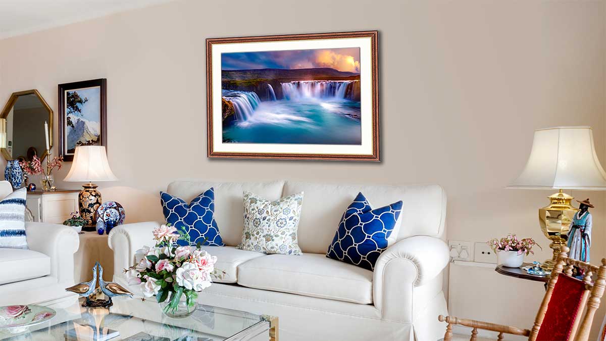 Landscape featuring an Icelandic waterfall, framed and hung in a sitting room with matching blue cushions.