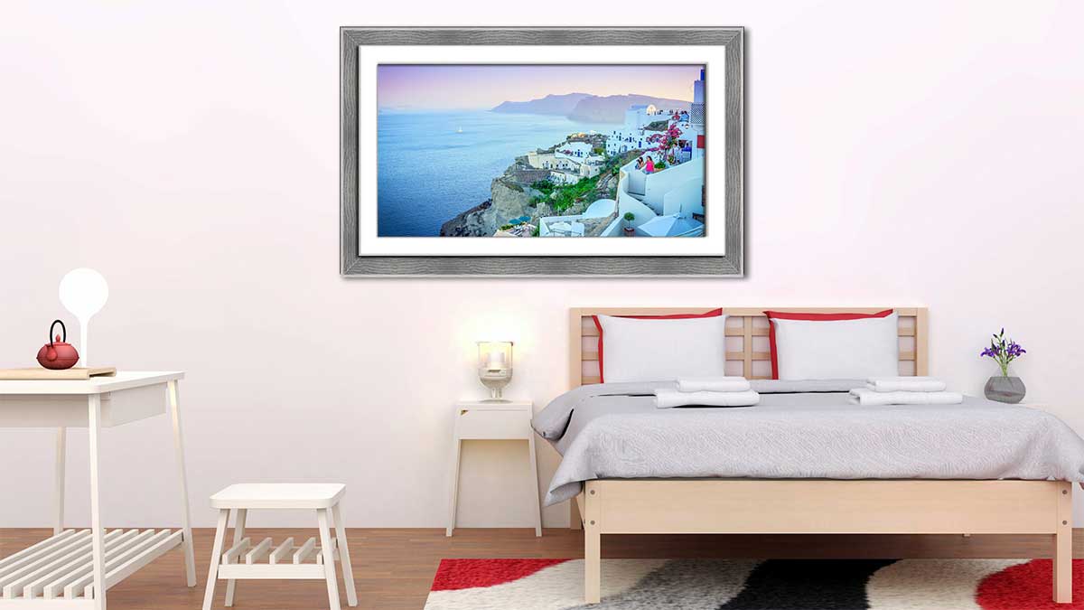 Sunset holiday snap of Santorini in Greece, framed in a grey open grain frame and hung in a minimalist styled bedroom with grey sheets on the bed and a grey rug.