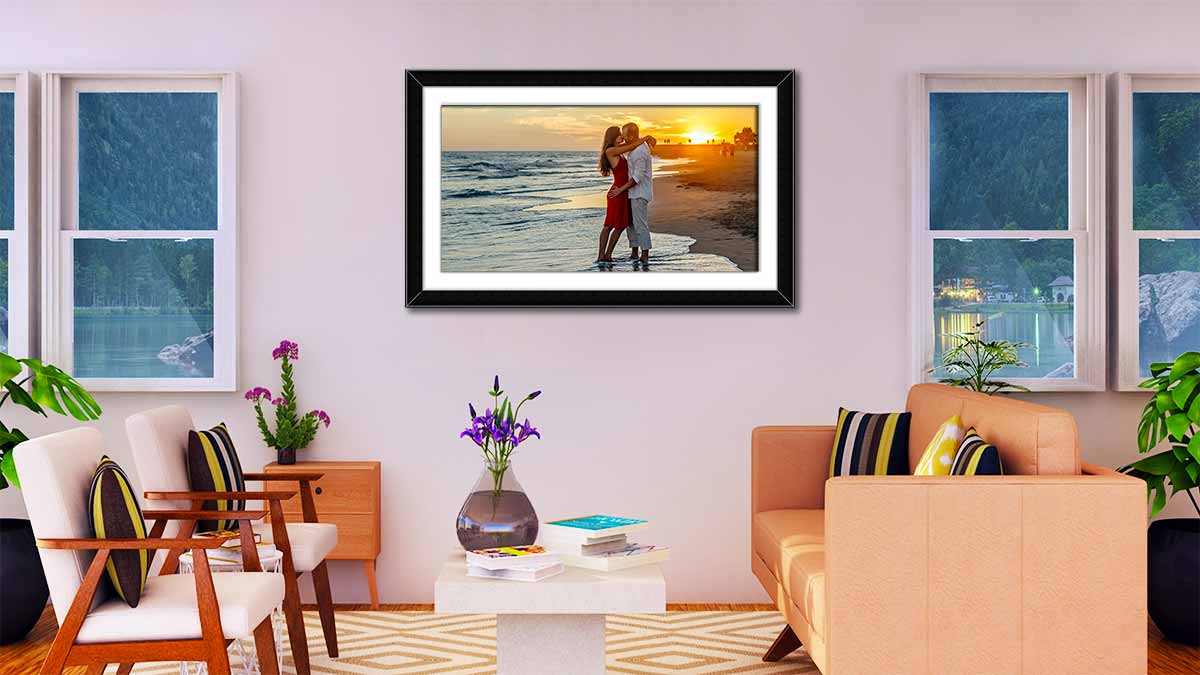 Photo of a honeymoon couple kissing in the sunset on a tropical beach. Panoramic poster framed in a simple black frame with mount and then hung between two windows in the reception area