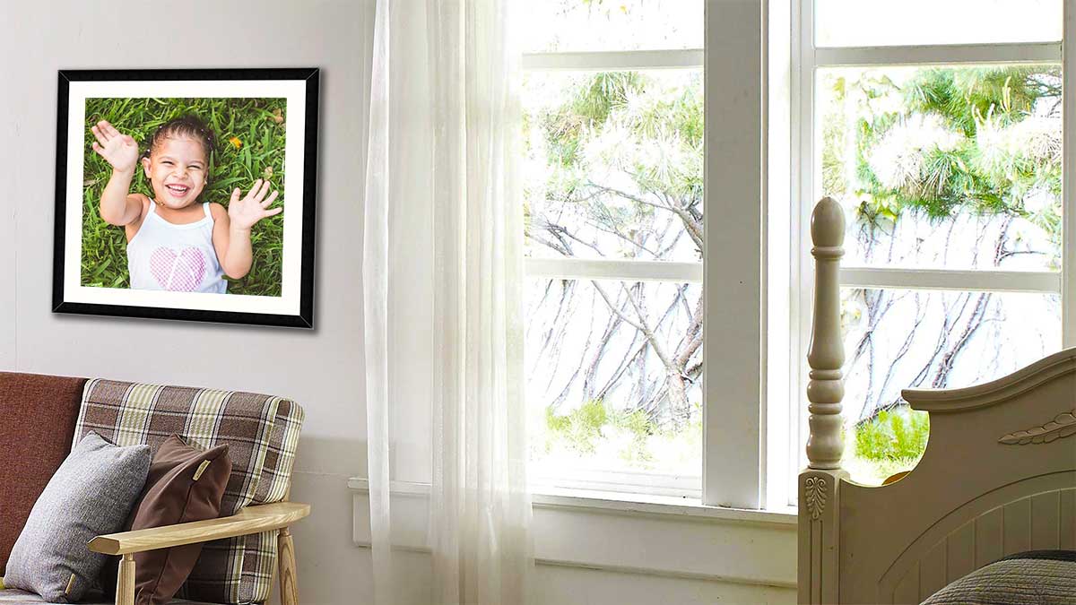 Photo of a child lying in the grass, laughing and smiling. Framed in a large black frame and hung by a window.