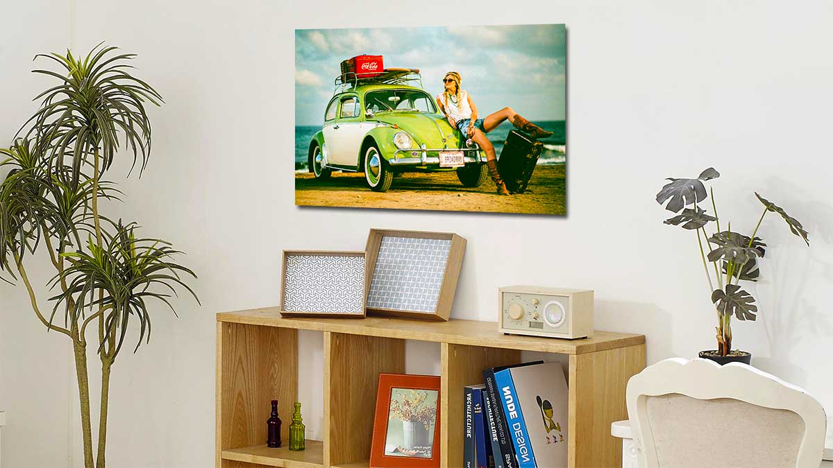 Photo of a VW bug on a beach with a woman posing on the bonnet. Poster is printed in a classic digital camera size and hung on the wall above a bookcase.