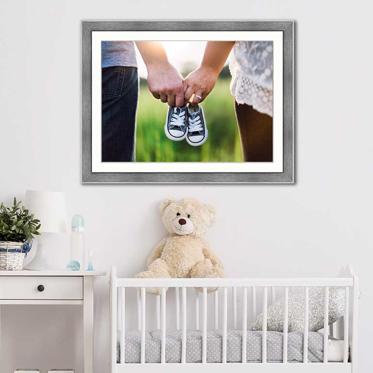 Photo of baby shoes in an A3 grey frame, hung above a crib with a teddy bear