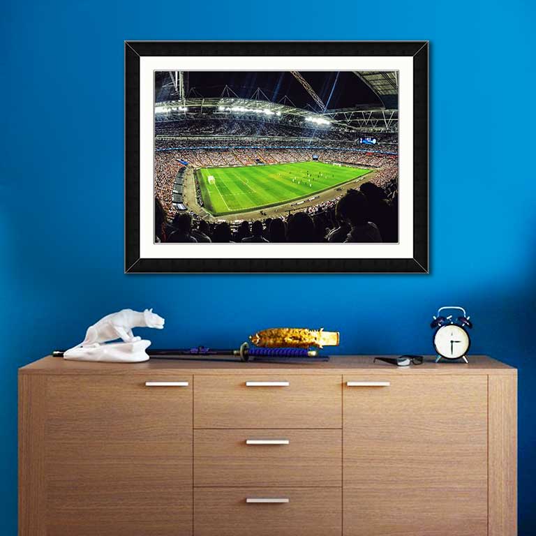 Photo of a football stadium during a game, framed in an A2 frame and hung over a sideboard.