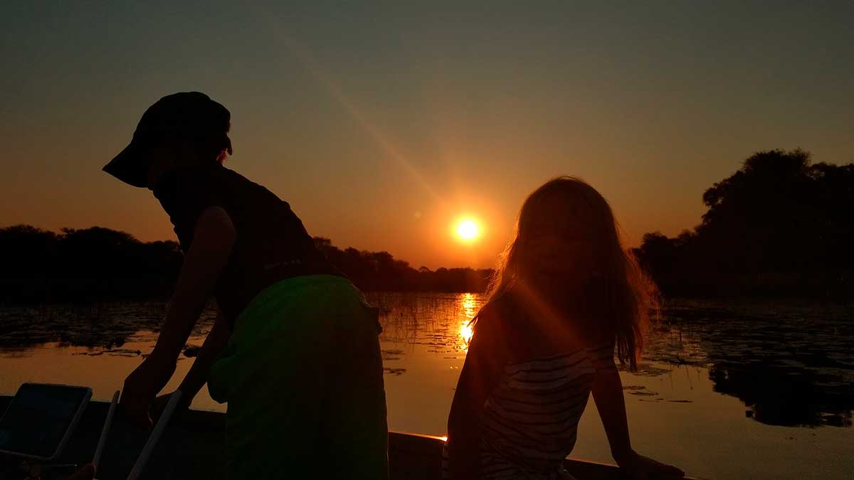 Picture of two children silhouetted in the sunset with their faces completely in shadow as they play by a river
