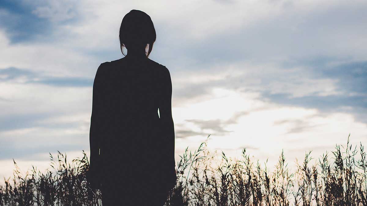 Photo of a woman silhouetted in the evening light as she stands within a field