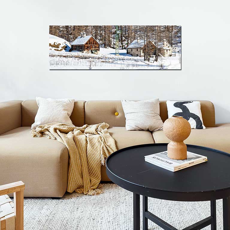 Poster of a winter holiday scene featuring cottages in the snow hung on a wall behind a plush sofa.
