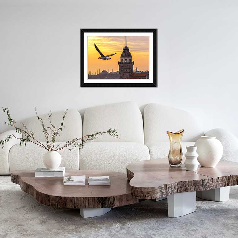 Picture frame featuring a photo of a bird flying in the sunset with the city behind hung in a modern living room