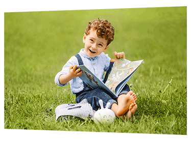 Poster print of a young boy sitting on the grass reading a book
